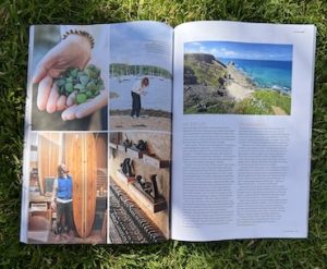 A close up image of National Geographic Traveller Magazine, page 115/116 showing Laura Polleys hands holding seaglass and her collecting seaglass on the waters edge with boats behind.  On the right hand page is the article text.